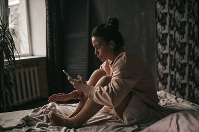 Side view of woman using mobile phone while sitting on bed