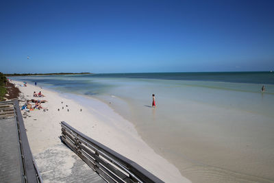 People enjoying at beach against clear blue sky