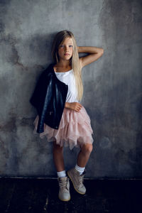 Fashionable girl model in a leather jacket skirt and shoes standing against the wall in the studio