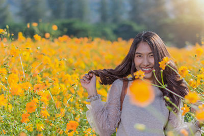 Portrait of smiling woman standing on yellow flowering plants