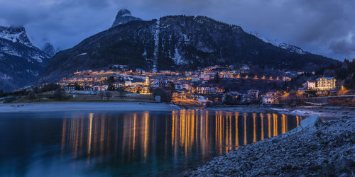 Illuminated buildings by mountains against sky at dusk