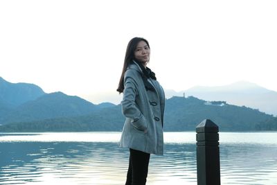 Portrait of smiling young woman standing by lake against sky