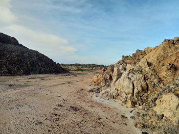 Dirt road amidst rocky mountains against sky