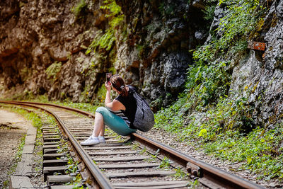 Woman photographing with phone while sitting on railroad track