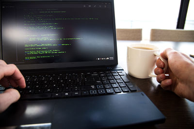 Cropped image of hands using laptop and holding coffee cup on table