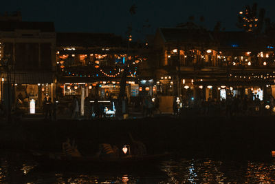 Illuminated buildings by river against sky at night