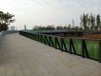 Railing by trees against sky in city