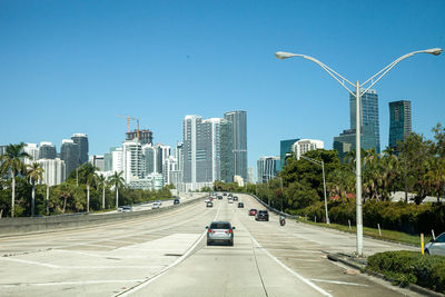 Cars on road by buildings against clear sky