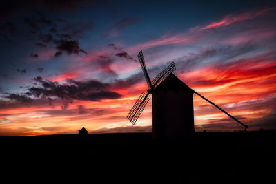 Silhouette traditional windmill on field against orange sky
