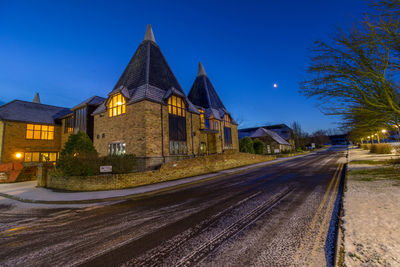 Illuminated street amidst buildings against blue sky at dusk