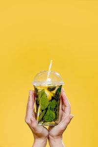 Close-up of hand holding drink against yellow background