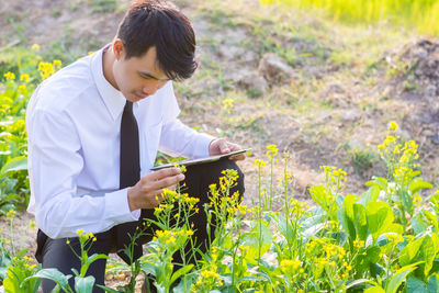High angle view of businessman holding digital tablet while looking at flower in park