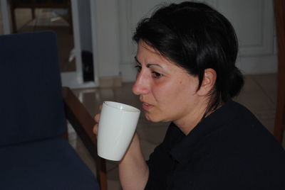 Side view of thoughtful woman with mug sitting at home