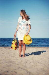 Woman holding umbrella on beach against sky