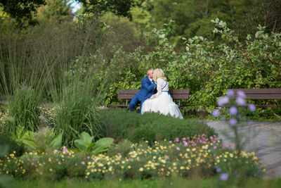 Newlywed couple kissing while sitting on bench at park