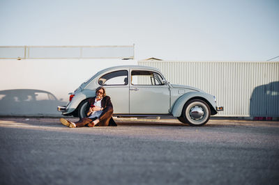 Senior man sitting in front of vintage car using mobile phone