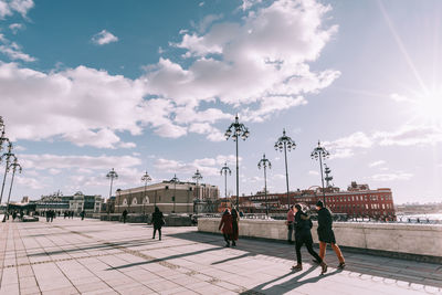 People walking on footpath in city against sky