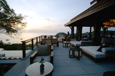 Chairs and tables by swimming pool against sky during sunset