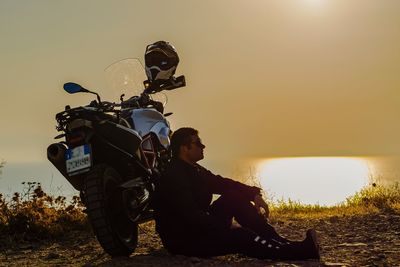 Side view of silhouette man sitting with motorcycle at beach against clear sky