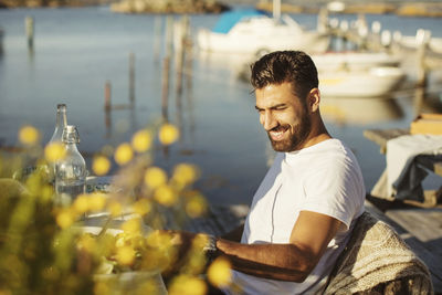 Smiling young man sitting on chair at table against lake