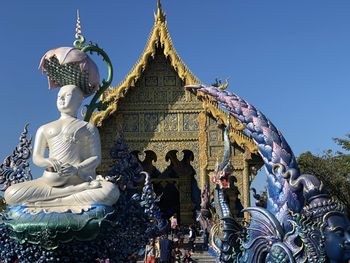 Low angle view of buddha statue at temple against clear blue sky