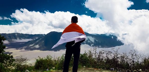 Rear view of man standing on mountain against sky