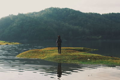 Woman standing at lakeshore against mountains