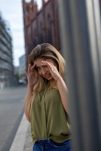Portrait of young woman gesturing while standing against buildings in city