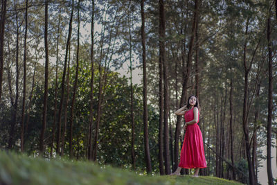 Side view of woman standing amidst trees in forest