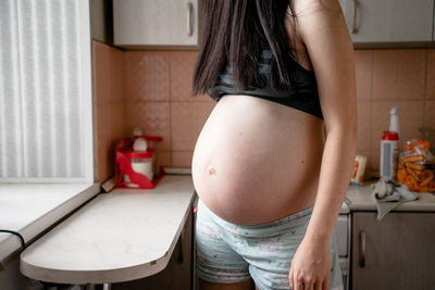 Midsection of pregnant women standing in kitchen