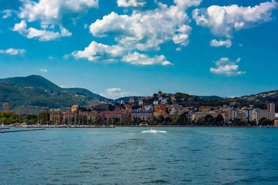 View of city at waterfront against cloudy sky