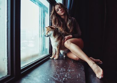 Young woman sitting with dog on window