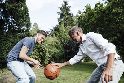 Father playing basketball with son in backyard during sunny day