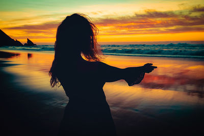 Silhouette woman with arms raised against sky during sunset