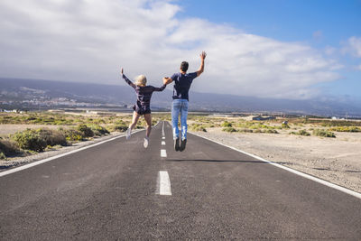 Rear view of young couple jumping on road against sky