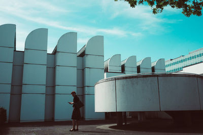 Side view of woman standing by building against sky