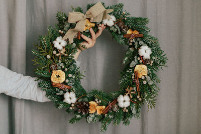 Cropped hand holding wreath against curtain