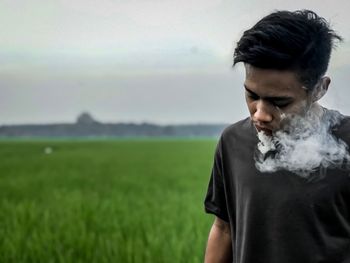 Young man smoking at agricultural field against sky