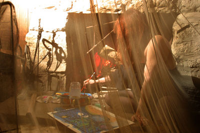 Woman making painting on canvas seen through curtain