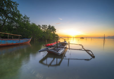 Boat moored in water against sky during sunset