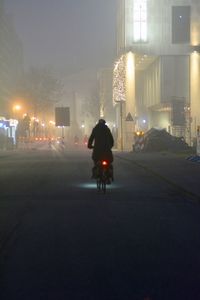 Rear view of man riding bicycle on road at night