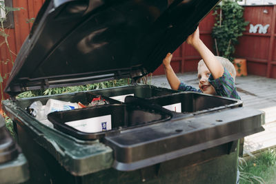 Boy opening recycling bin in garden