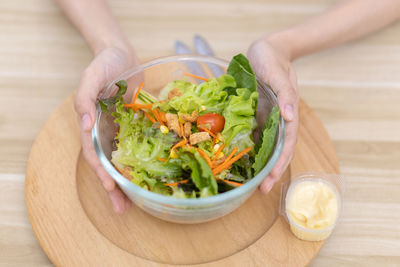 Cropped hand of woman holding salad in bowl on table