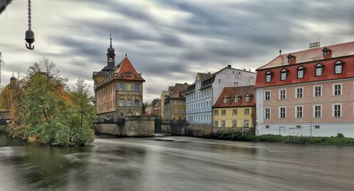 View of buildings by river against cloudy sky