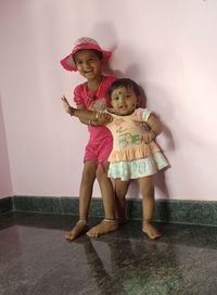 Cheerful sisters standing on floor against wall