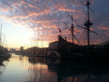 Sailboats moored at harbor against cloudy sky