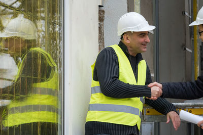 Engineers shaking hands while standing against wall