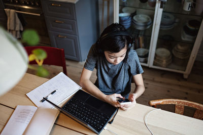 High angle view of studious boy using mobile phone for homework at table