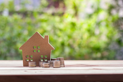 Close-up of cardboard model home with coins on wooden table against plants