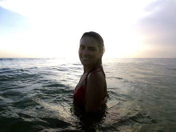 Portrait of young woman in sea against sky during sunset